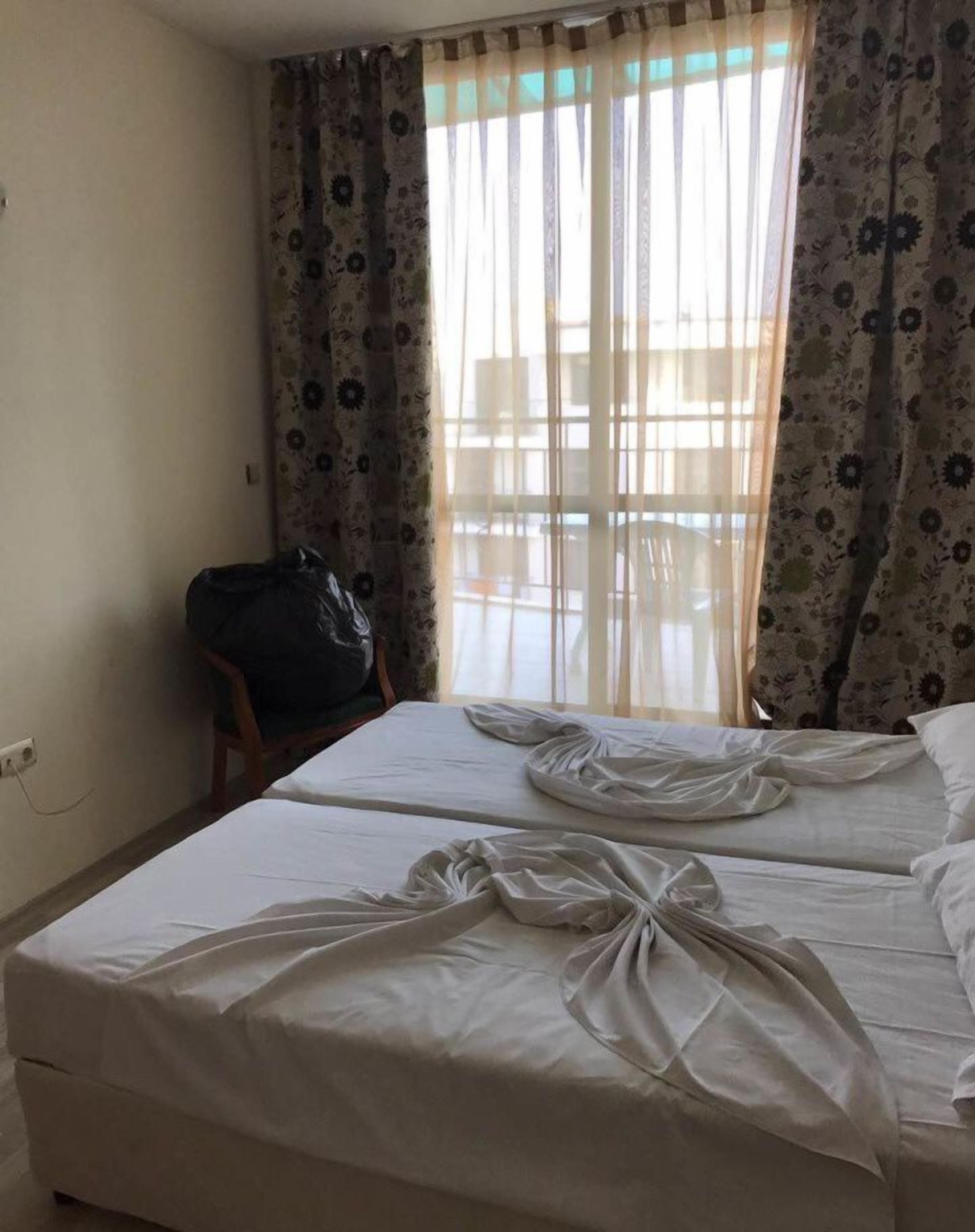 A hotel room with two beds, a chair, and a large window with floral curtains.