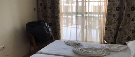 A hotel room with two beds, a chair, and a large window with floral curtains.