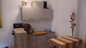 Eine kompakte Küche mit Mikrowelle, Toaster und Kaffeemaschine auf der Arbeitsfläche, einem kleinen Spülbecken und einem Esstisch mit zwei Stühlen.