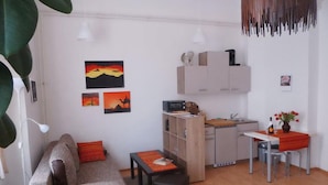 Ein kompakter Wohnraum mit Sofa, einem kleinen Esstisch, einer Küchenzeile und Bildern an den Wänden.