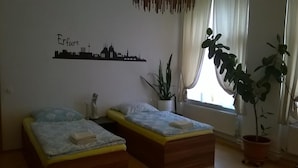 Ein Schlafzimmer mit zwei Einzelbetten, einer Wandmalerei mit Stadtansicht, einer Topfpflanze und einem Fenster mit Vorhängen.