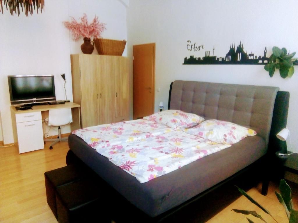 Ein Schlafzimmer mit einem Bett, einem Schreibtisch, einem Fernseher und einer Wanddekoration mit Stadtansicht.