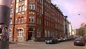 Eine Reihe geparkter Autos entlang einer Straße mit einem rot Backsteinhaus mit Rundbogenfenstern und einem Schild mit der Aufschrift 'P'.
