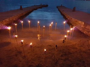 A beach at night with torches arranged in a circle, a pier extending into the water, and a rocky shoreline. - Villa Jadranka Privlaka (Privlaka)
