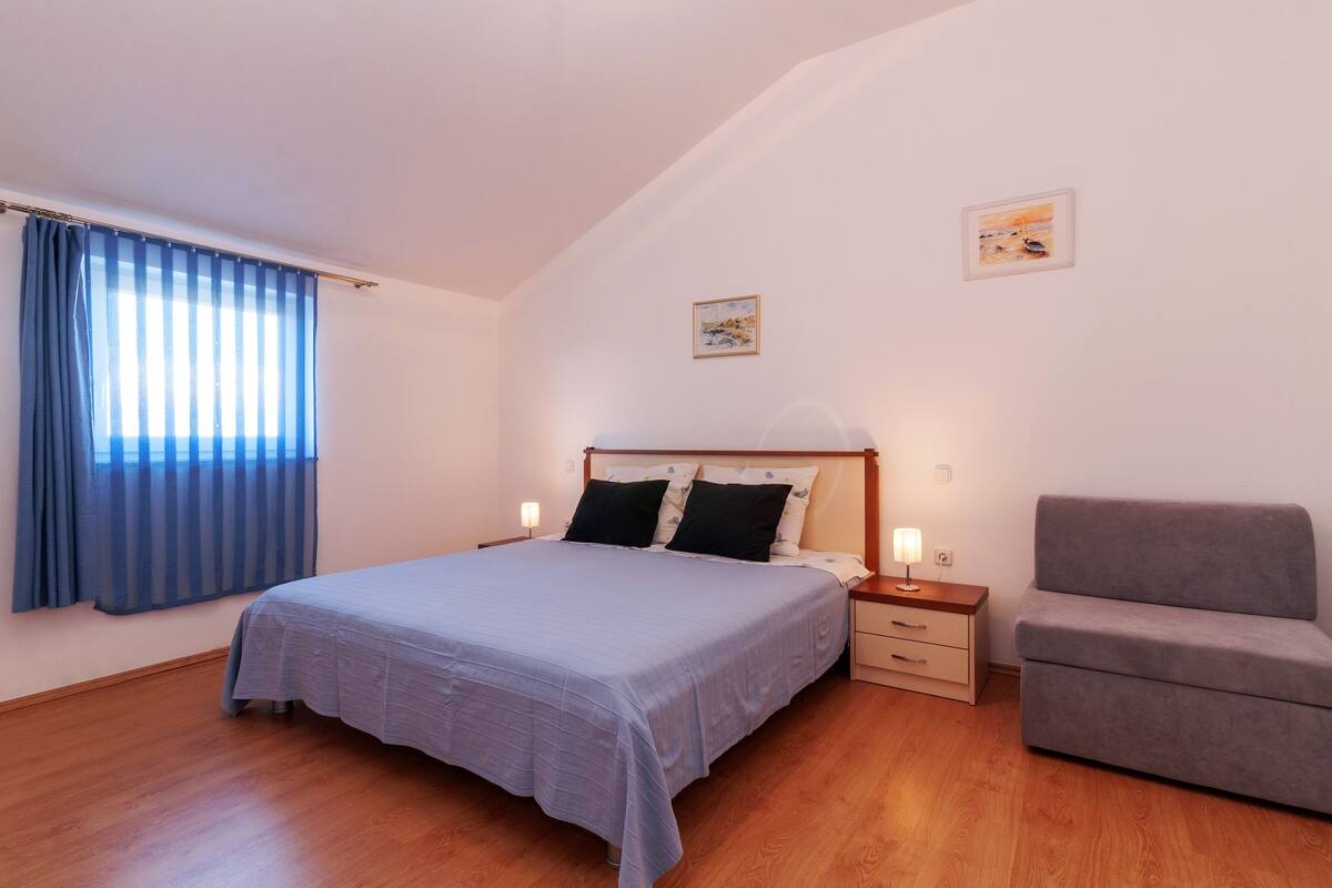 A bedroom with a bed, bedside tables, a chair, and a painting on the wall.