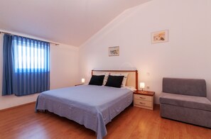 A bedroom with a bed, bedside tables, a chair, and a painting on the wall. - Villa Jadranka Privlaka (Privlaka)