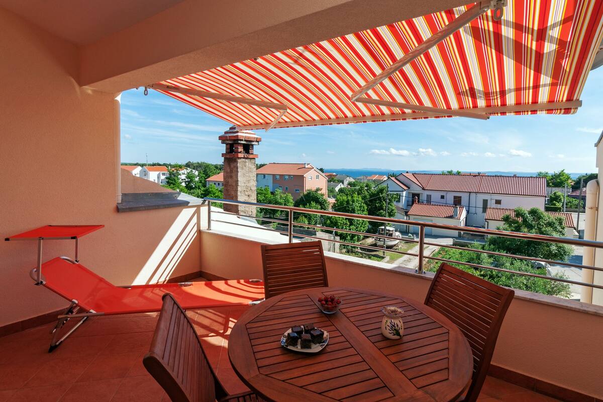 A balcony with a red-striped umbrella, a wooden table, and a red lounge chair.