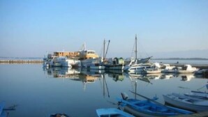 Un puerto deportivo con varias embarcaciones amarradas, un edificio de techo inclinado y agua tranquila que refleja los barcos.