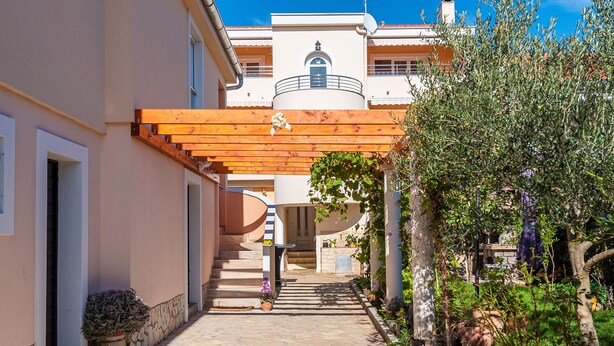 Un camino empedrado que lleva a un edificio con una pérgola de madera y plantas en macetas.