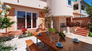 Un comedor exterior moderno con una mesa de madera, platos azules y un vaso transparente.