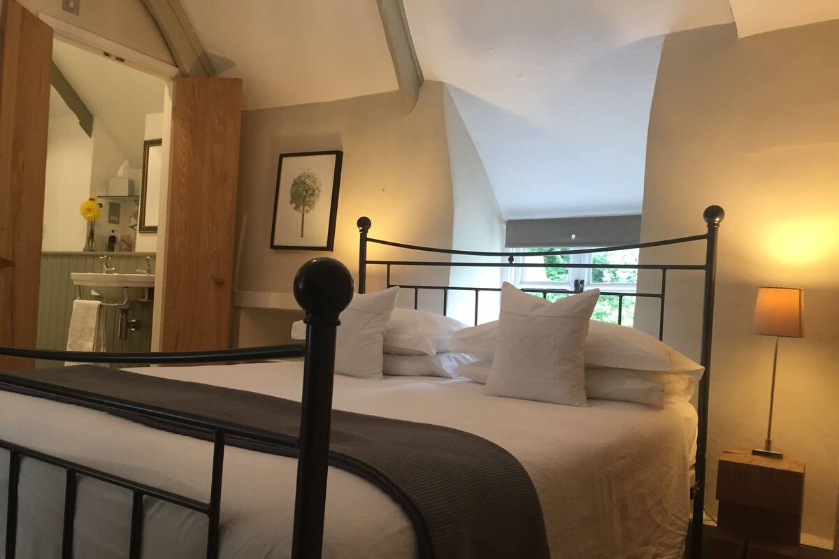 A bedroom with a four-poster bed, a bedside table, a lamp, and a view of the bathroom.