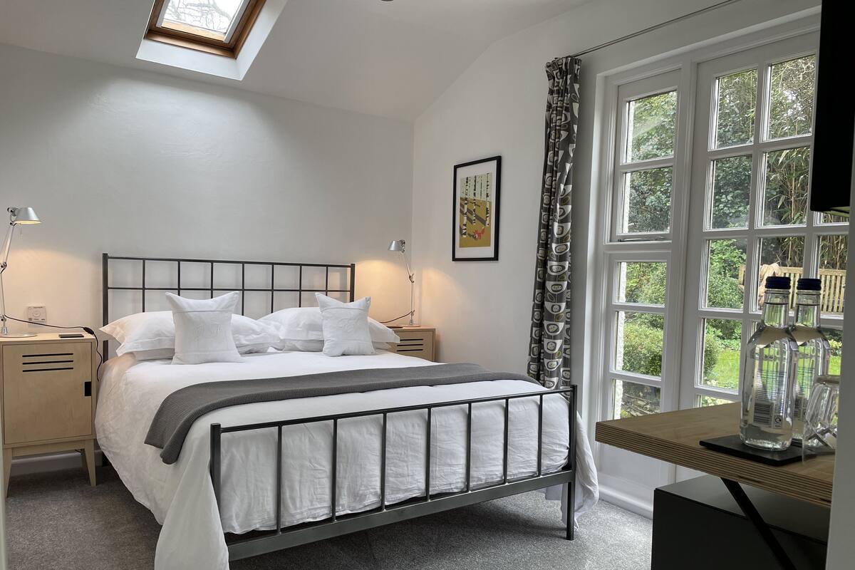 A neatly arranged bedroom with a bed, bedside tables, a desk, and a window with curtains.