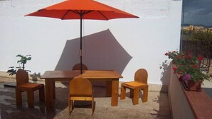 An outdoor patio with a wooden table and chairs, a red umbrella, and potted plants.