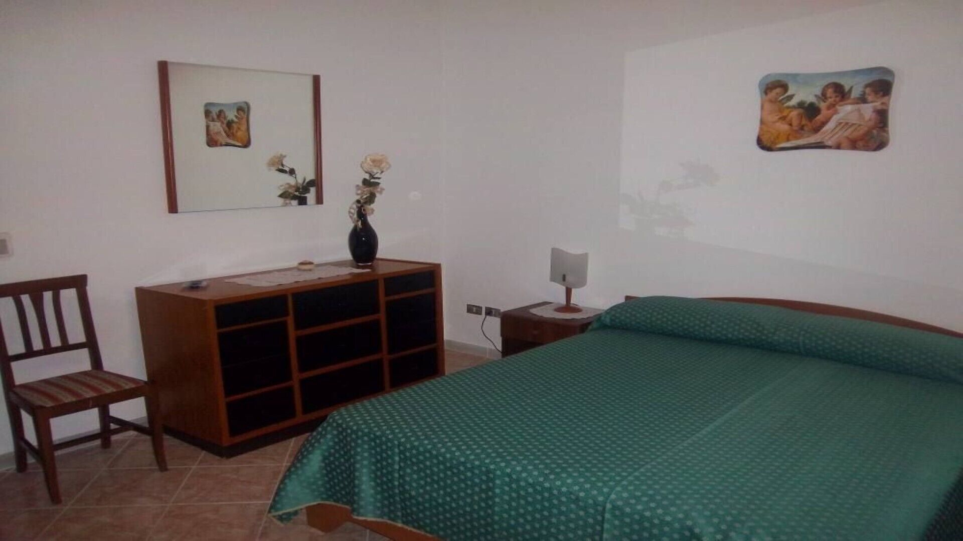 Une chambre à coucher comprenant un lit, une commode en bois, une chaise et deux tableaux accrochés au mur.