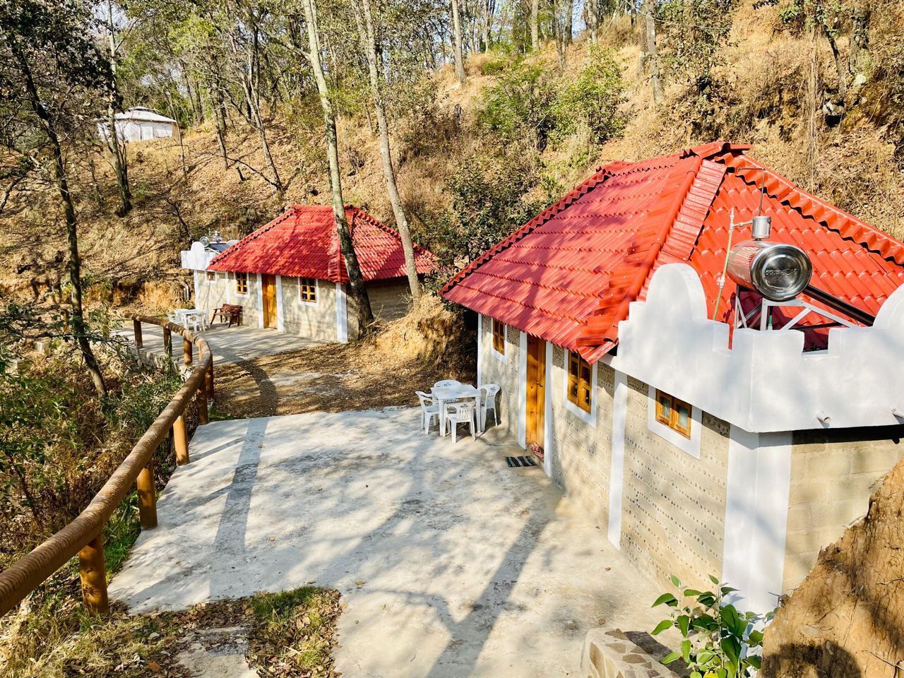 Una cabaña rústica con techo rojo, un camino de hormigón que lleva a la entrada y una pequeña zona de estar al aire libre.