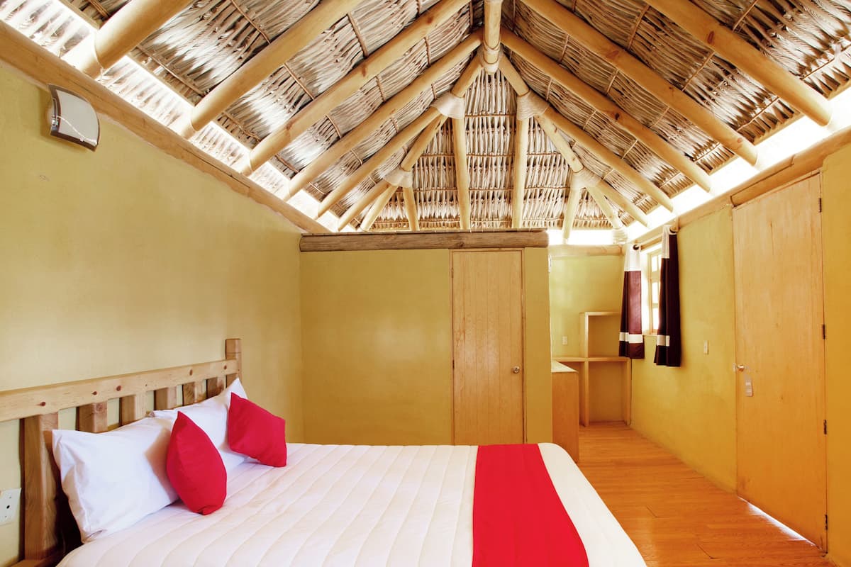 A bedroom with a wooden ceiling, a bed with white and red bedding, and wooden walls.
