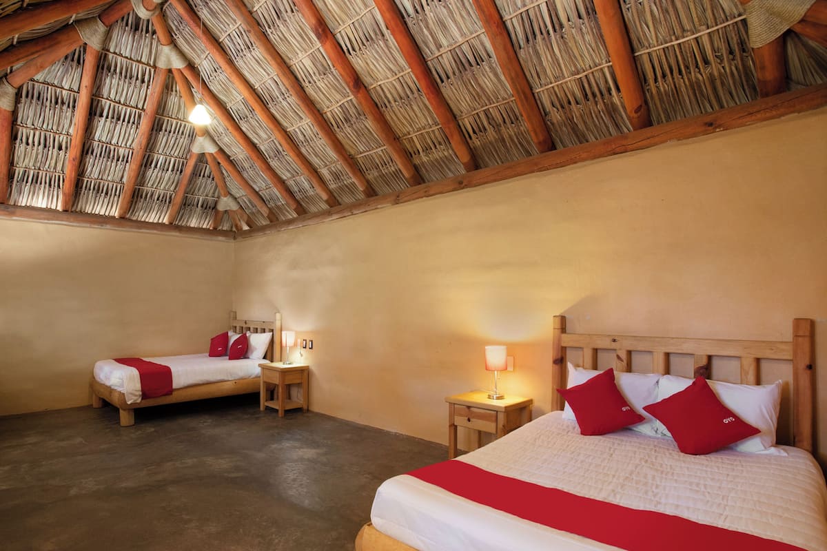A room with two beds, a thatched roof, and a concrete floor.