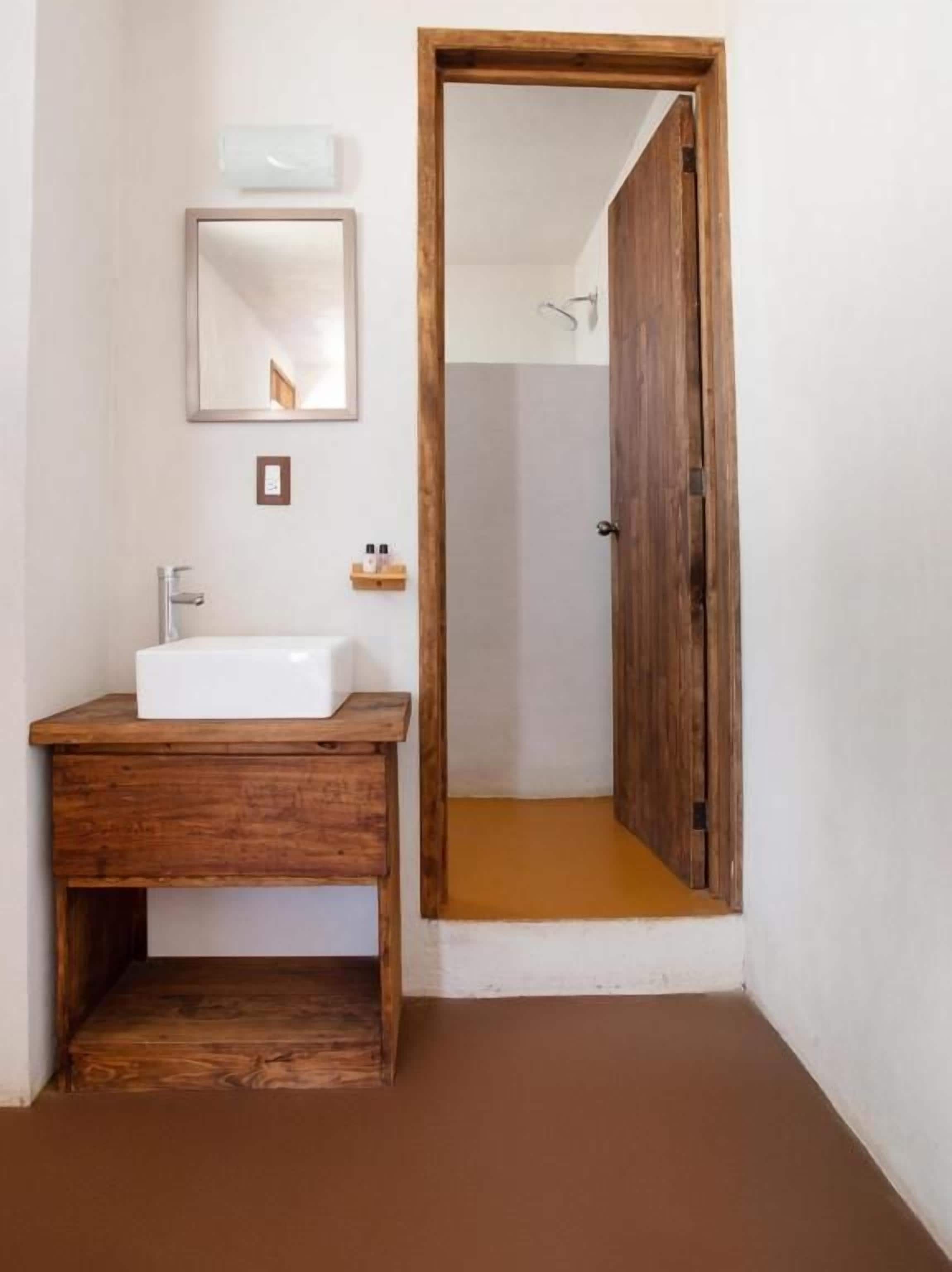 A bathroom with a wooden vanity, a mirror, and a shower area visible through an open door.