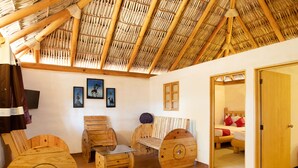Una habitación rústica con muebles de madera, techo de paja y una cama con almohadones rojos.