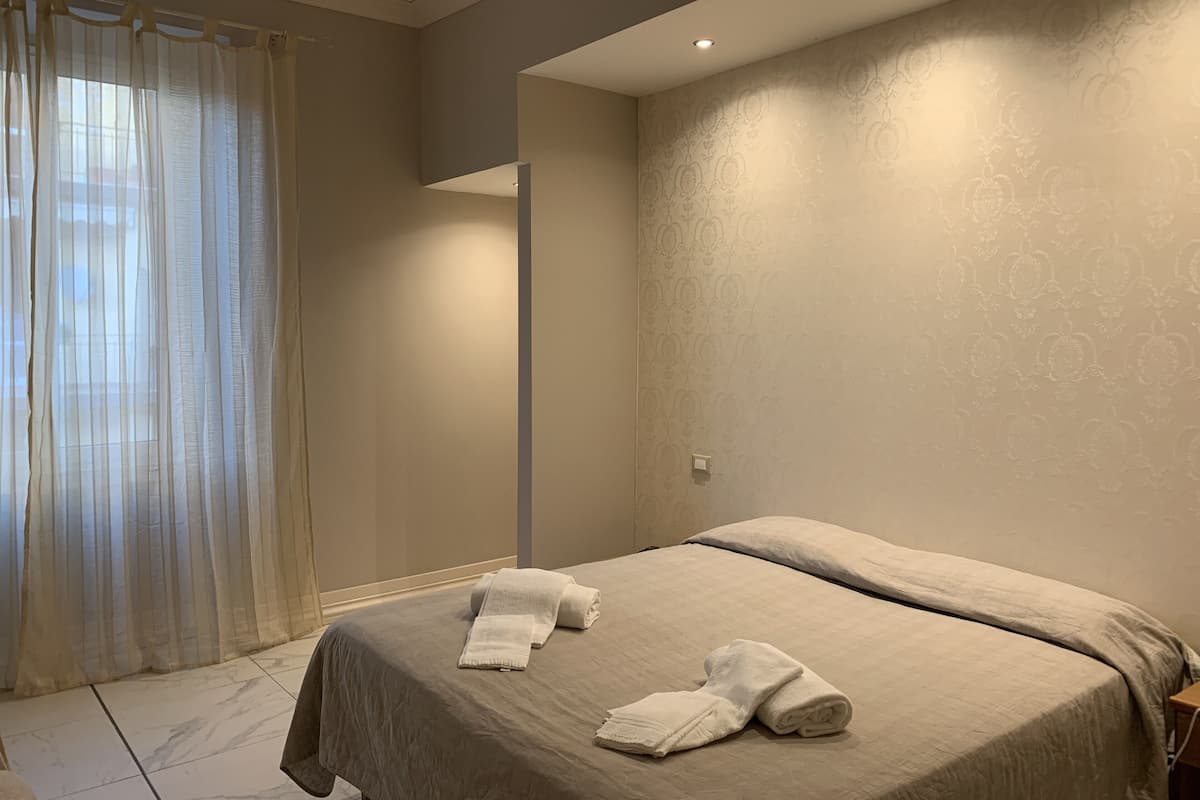 A bedroom with a bed, a window with sheer curtains, and a patterned wall.