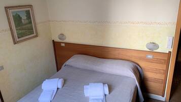A neatly made bed with two towels, a wooden headboard, a wall-mounted light fixture, and a framed picture.
