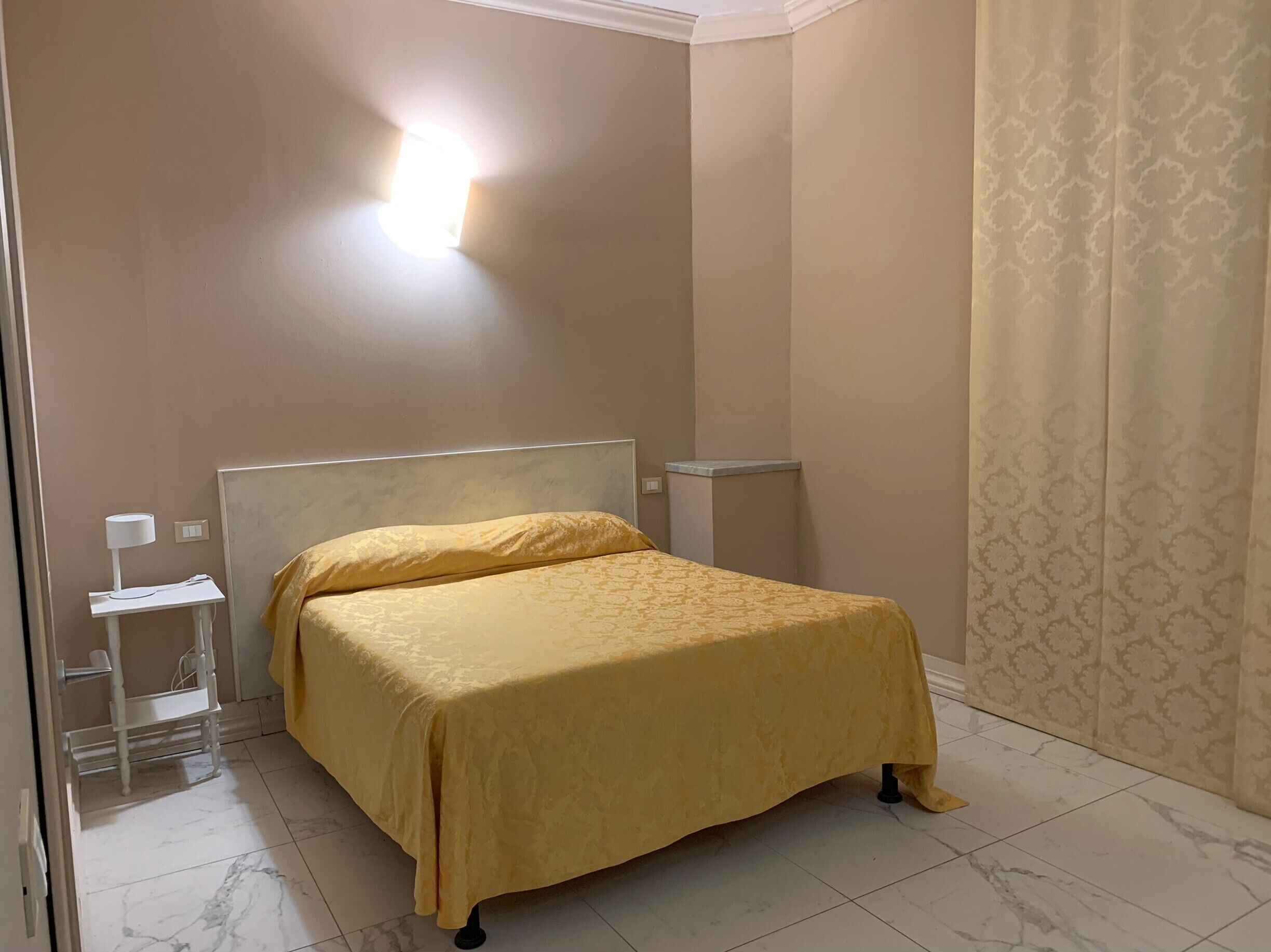 A hotel room with a bed, a bedside table with a lamp, and a wall-mounted light fixture.