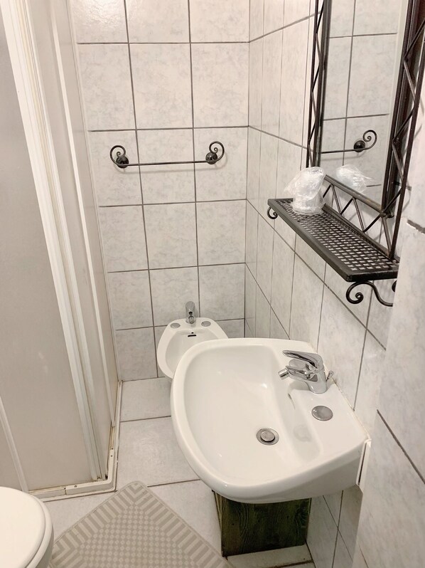 A bathroom with two urinals, a sink, and a metal shelf with plastic bags. - Albergo La Villetta (Sarzana)