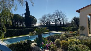 Une piscine entourée de haies bien entretenues et de diverses plantes, sous un ciel bleu dégagé.