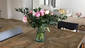 Une table à manger avec un vase de fleurs au centre, une chaise en bois et un canapé blanc en arrière-plan.