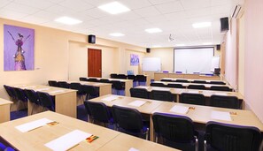 Une salle de classe avec des rangées de bureaux et de chaises, un tableau blanc et un écran de projection.