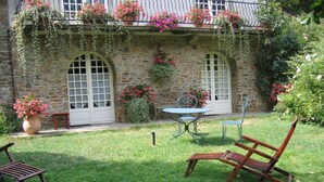 Um edifício de pedra com janelas em arco, um pátio com mesa e cadeiras, e cestos com flores penduradas.