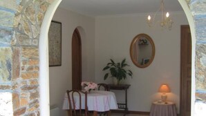 Uma área de refeições com um arco de pedra, uma mesa com cadeiras, um vaso de planta, um espelho e um abajur.