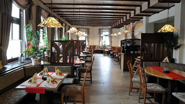 Un restaurante con mesas y sillas de madera, lámparas colgantes y plantas en macetas.