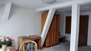 Una habitación con un escritorio de madera, una silla, una mesita con un florero y un armario.
