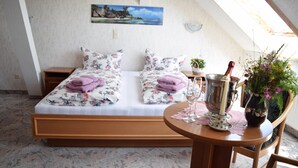 Un dormitorio con una cama grande, una mesita de noche de madera, una pequeña mesa con un jarrón y una botella, y un cuadro en la pared.