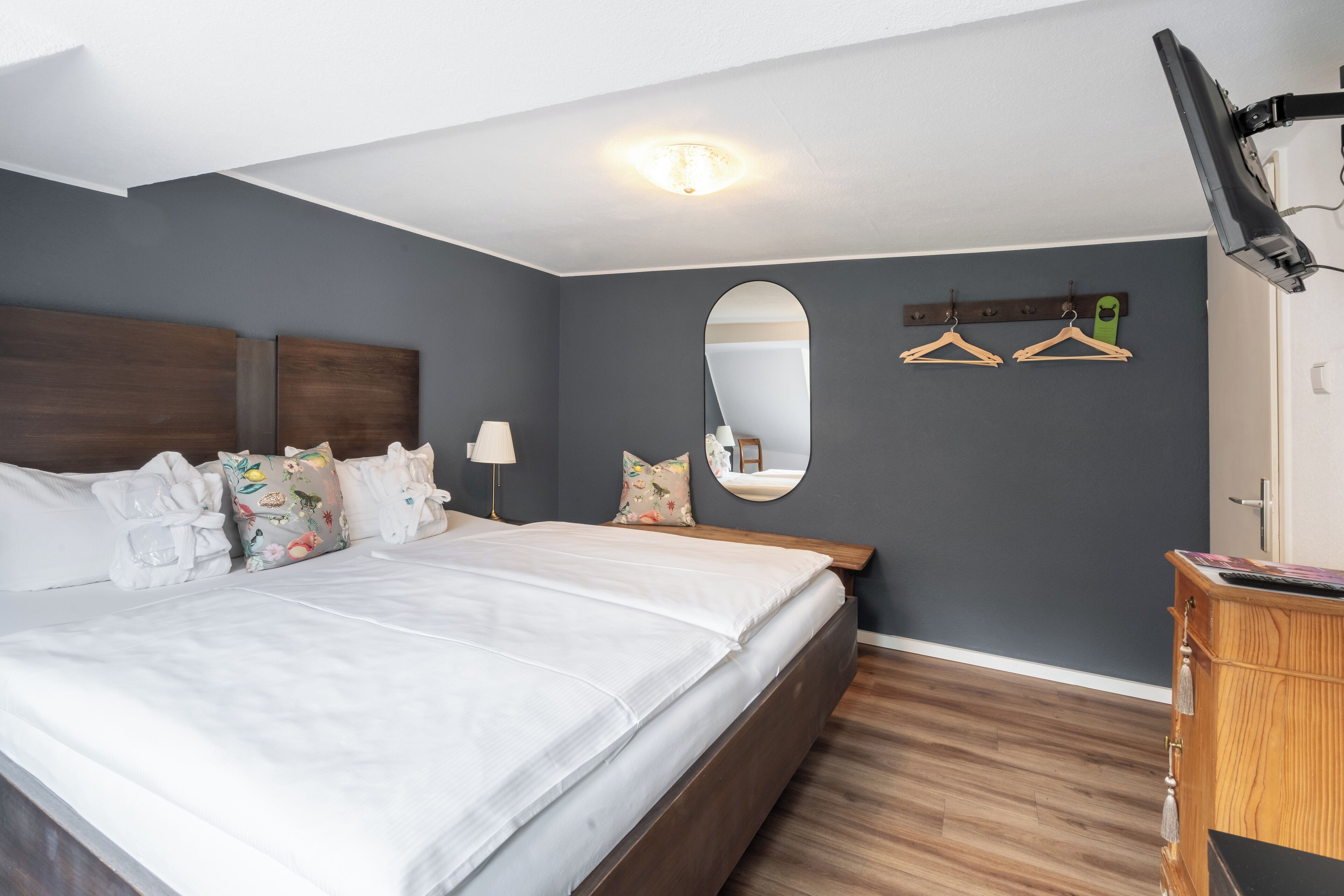 A bedroom with a large bed, a wooden dresser, a mirror, and a TV mounted on the wall.