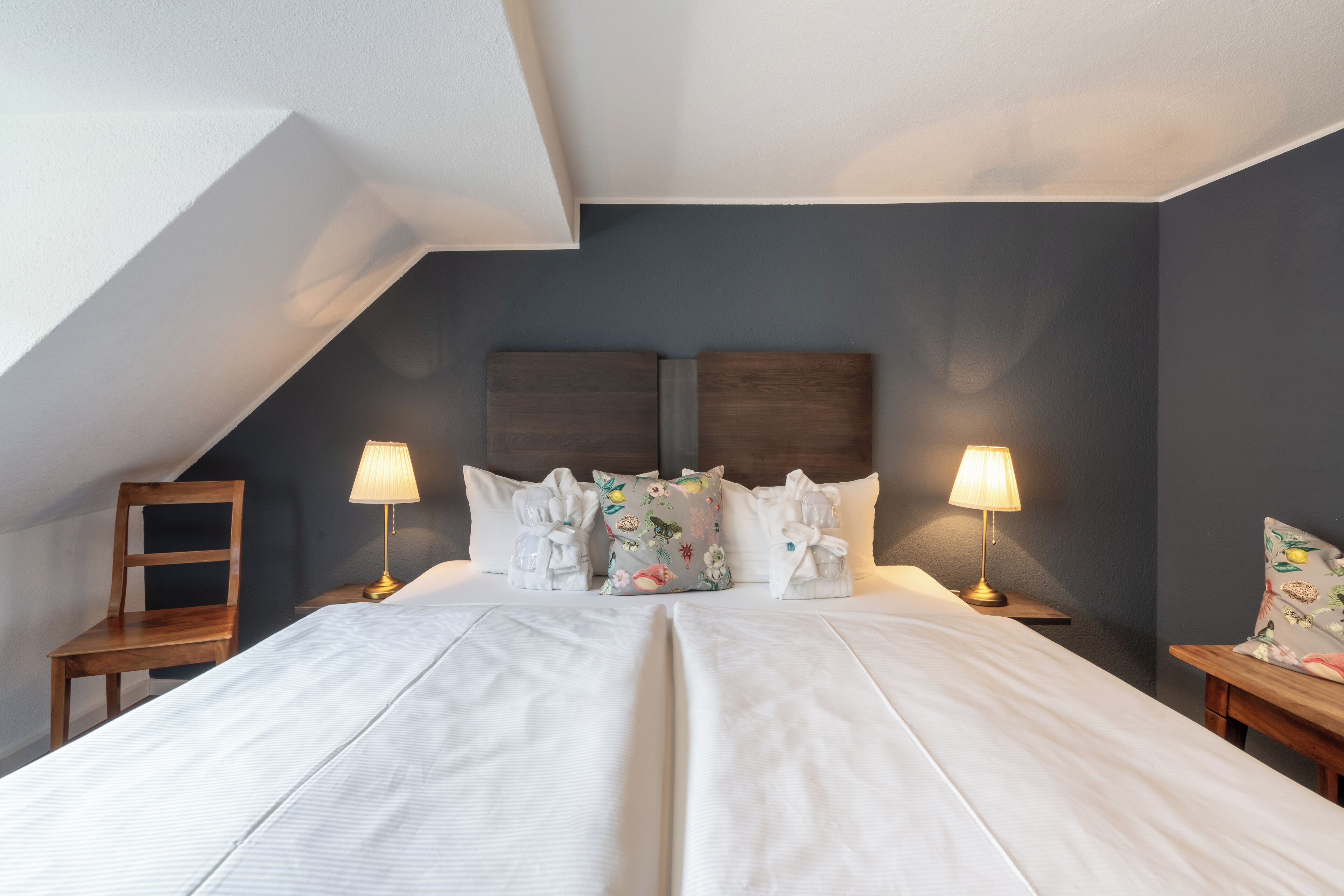 Ein Schlafzimmer mit einem großen Bett, zwei Nachttischen, einem Holzstuhl und einer geneigten Decke.
