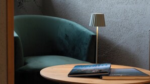 A room with a green armchair, a round wooden table with a book, and a floor lamp. - Hotel am Fischmarkt (Konstanz)