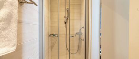 A glass-enclosed shower with a handheld showerhead and a wall-mounted faucet.