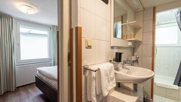 Une chambre d’hôtel avec un lit, une salle de bain comprenant un lavabo, un miroir et une douche.