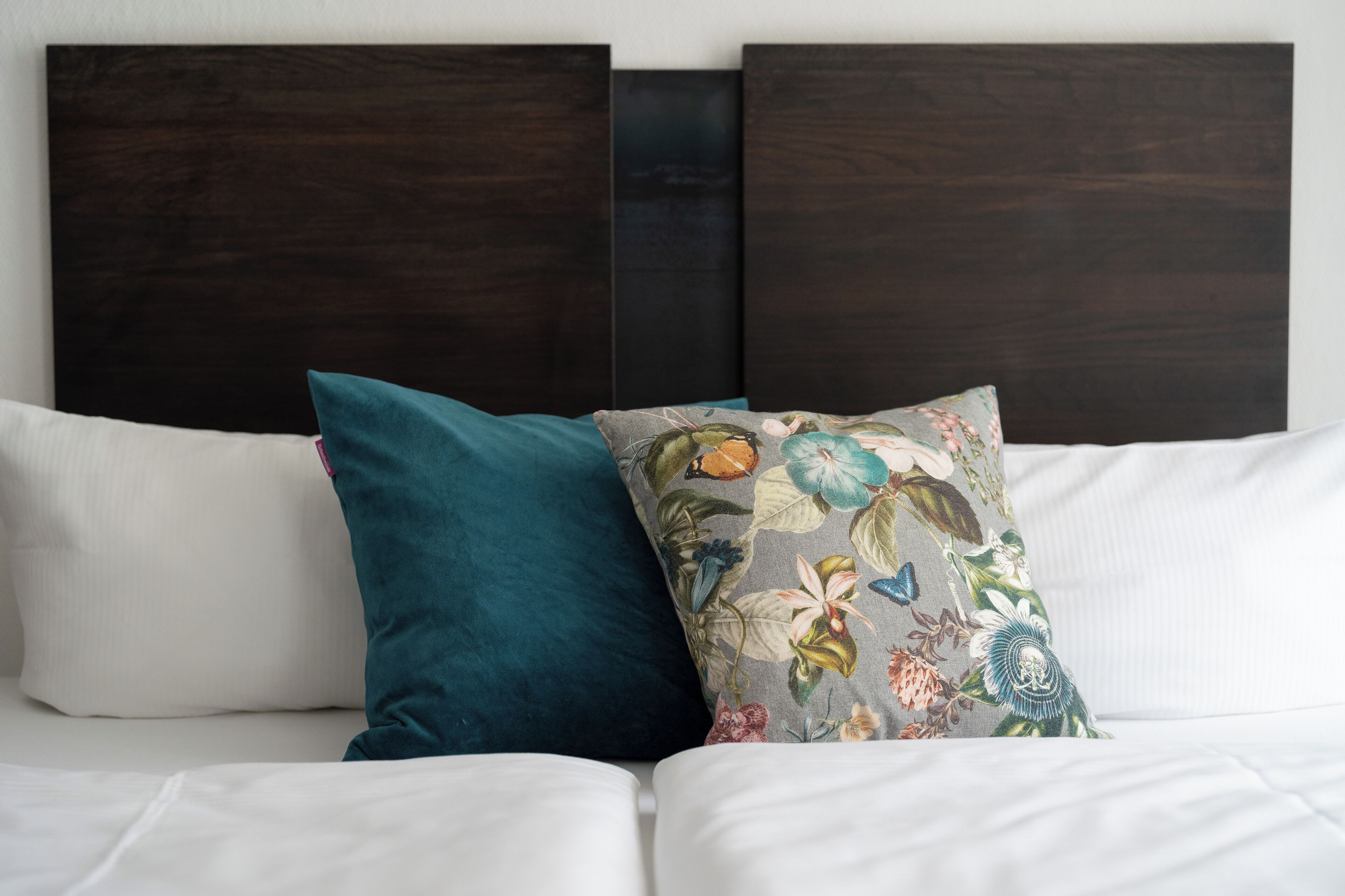 A bed with white bedding and two pillows, one teal and one with a floral pattern.