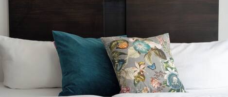 A bed with white bedding and two pillows, one teal and one with a floral pattern.