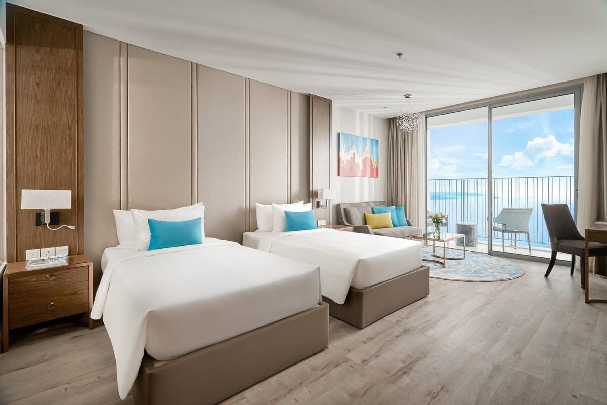 A hotel room with two beds, a balcony with a view, and a desk with a chair.