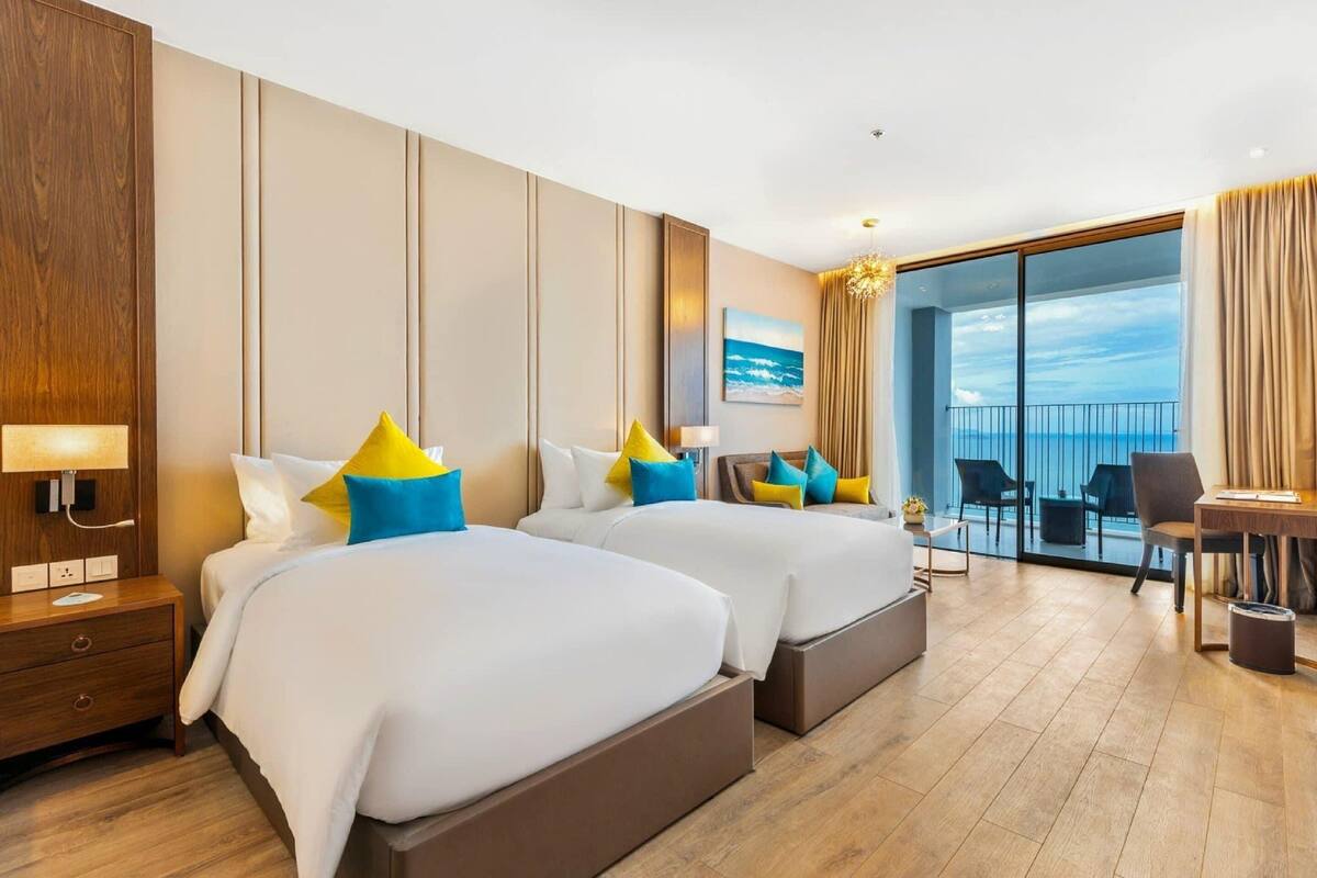 A hotel room with two beds, a desk, a chair, and a balcony with a view.