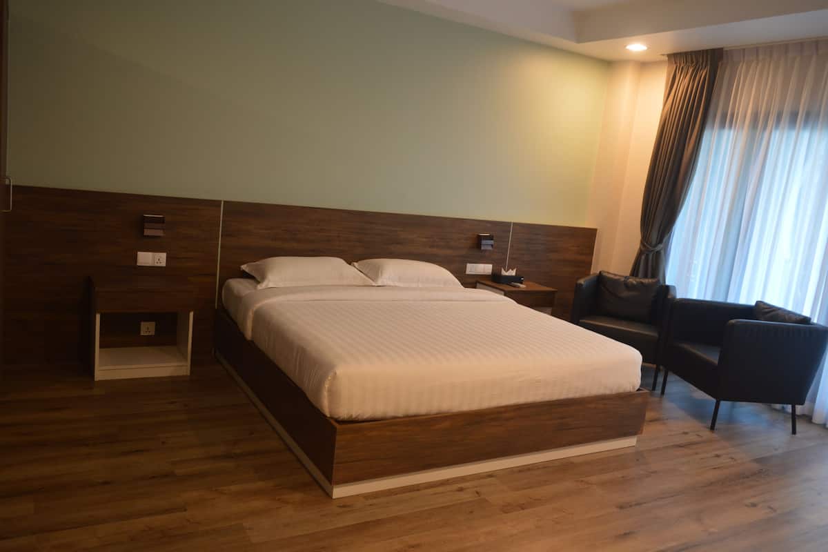 Una habitación de hotel moderna con una cama grande, una mesita de noche, una silla y una ventana con cortinas.