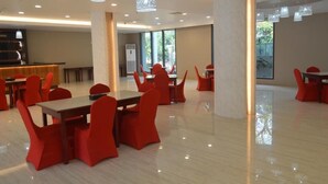 Un comedor espacioso con sillas y mesas rojas, ventanas amplias e iluminación colgante moderna.