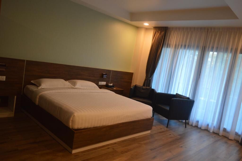 A hotel room with a large bed, a bedside table, a chair, and a window with curtains.