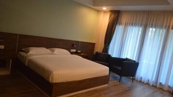 A hotel room with a large bed, a bedside table, a chair, and a window with curtains.