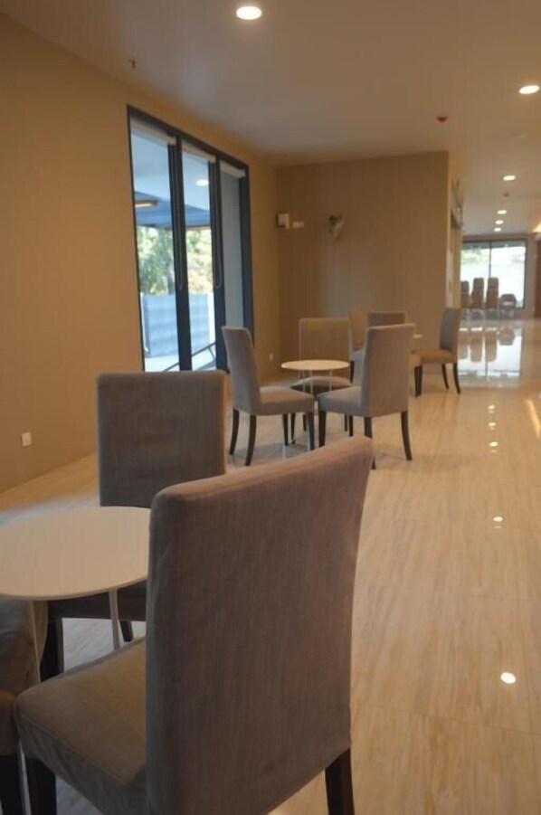 A modern hotel lobby with a long corridor, seating areas with tables and chairs, and large windows offering views.