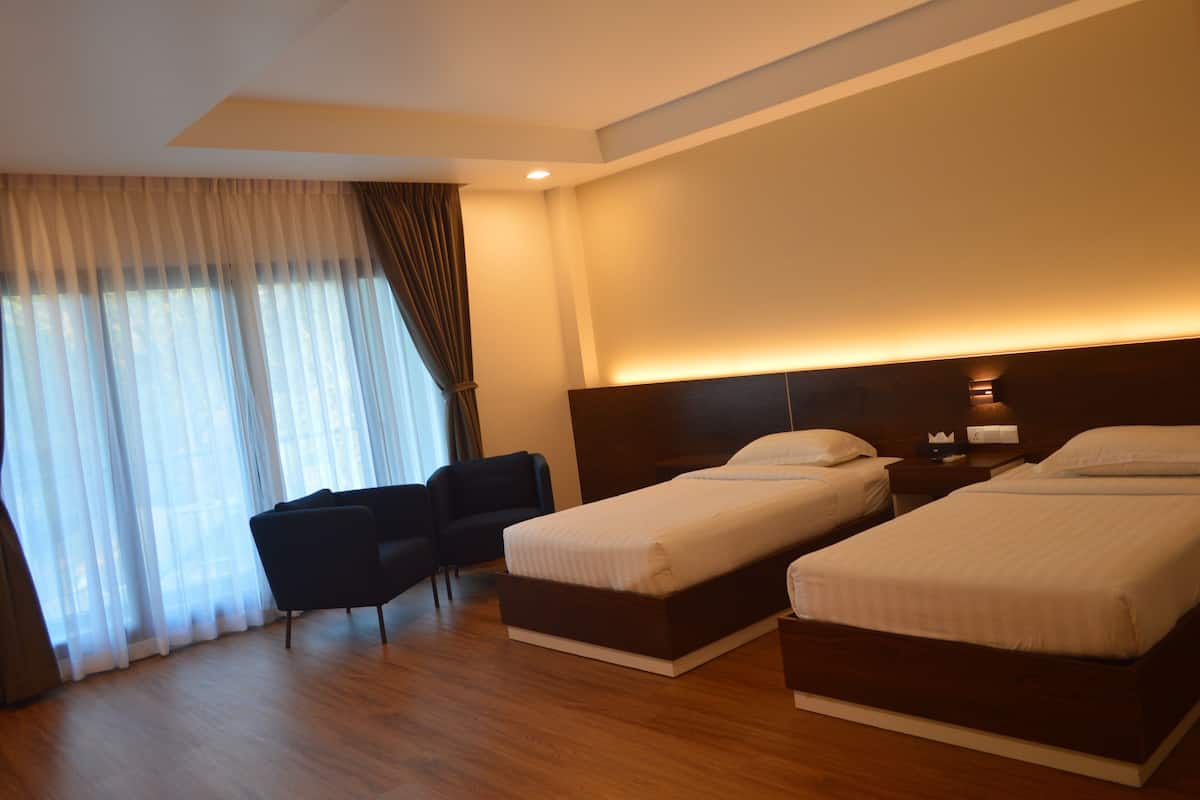 Habitación de hotel con dos camas individuales, un escritorio, una silla y un ventanal con cortinas.